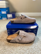 Pair of gray suede clogs on a blue shoe box with a blurred background